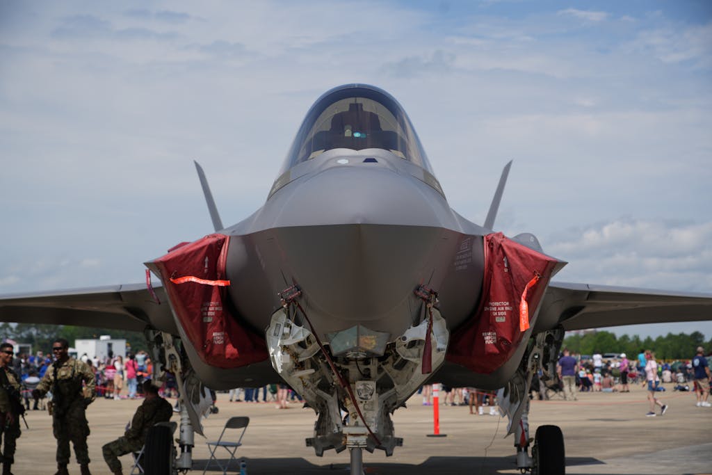 Front view of an F-35 fighter jet on display at an airshow in Hampton, Virginia with military personnel nearby.